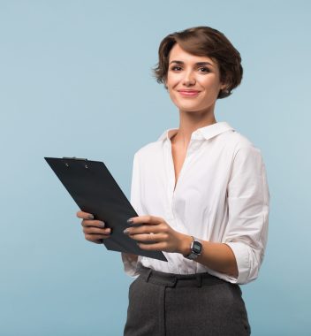 hermosa-mujer-negocios-cabello-corto-oscuro-camisa-blanca-sosteniendo-carpeta-negra-manos-mientras-mira-alegremente-camara-sobre-fondo-azul-scaled.jpg